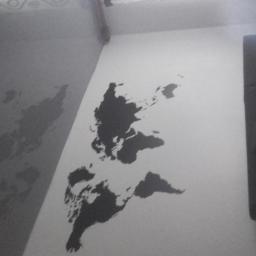 Sufity napinane sufit design - Ściana z namalowaną czarną mapą świata, widoczny fragment narożnika i sofy, słabe oświetlenie.