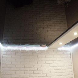 Sufity napinane sufit design - Częstochowa: Fragment pomieszczenia z czarnym, lustrzanym sufitem i oświetleniem LED, biała ściana z cegły oraz podwieszany sufit z halogenami.