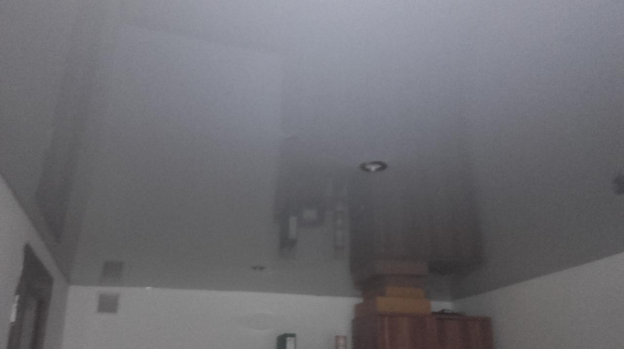 Błyszczący, szary sufit napinany z widocznym oświetleniem punktowym w rogu pokoju.