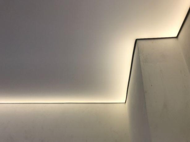 Nowoczesny sufit z ukrytym oświetleniem LED wzdłuż krawędzi, tworzący delikatną poświatę na ścianach.