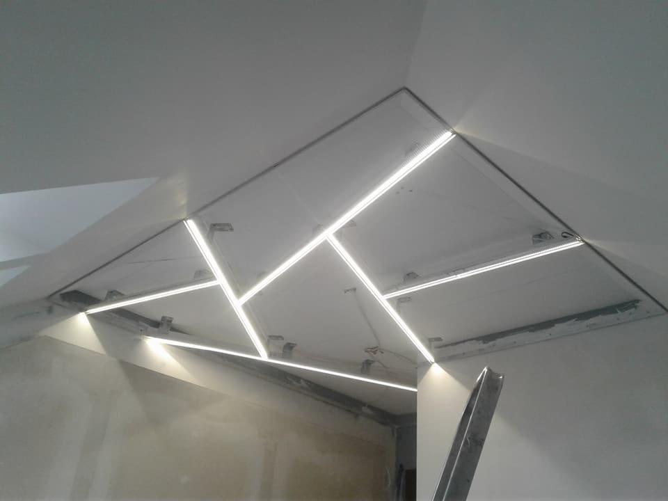 Nowoczesny sufit z podświetleniem LED w kształcie geometrycznym, widoczne elementy montażowe i niedokończone wykończenie ścian.