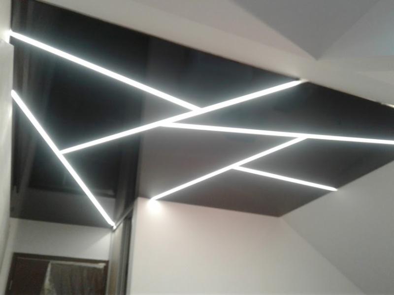 Czarny sufit podwieszany z geometrycznym wzorem z białych, liniowych lamp LED, w narożniku widoczny fragment drzwi.