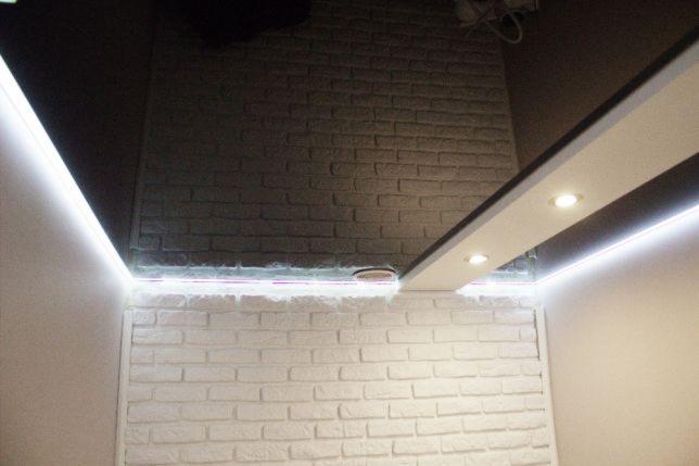 Częstochowa: Fragment pomieszczenia z czarnym, lustrzanym sufitem i oświetleniem LED, biała ściana z cegły oraz podwieszany sufit z halogenami.