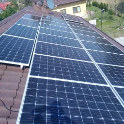 Panele słoneczne zamontowane na brązowym dachu domu jednorodzinnego z anteną satelitarną, widok z góry w słoneczny dzień.