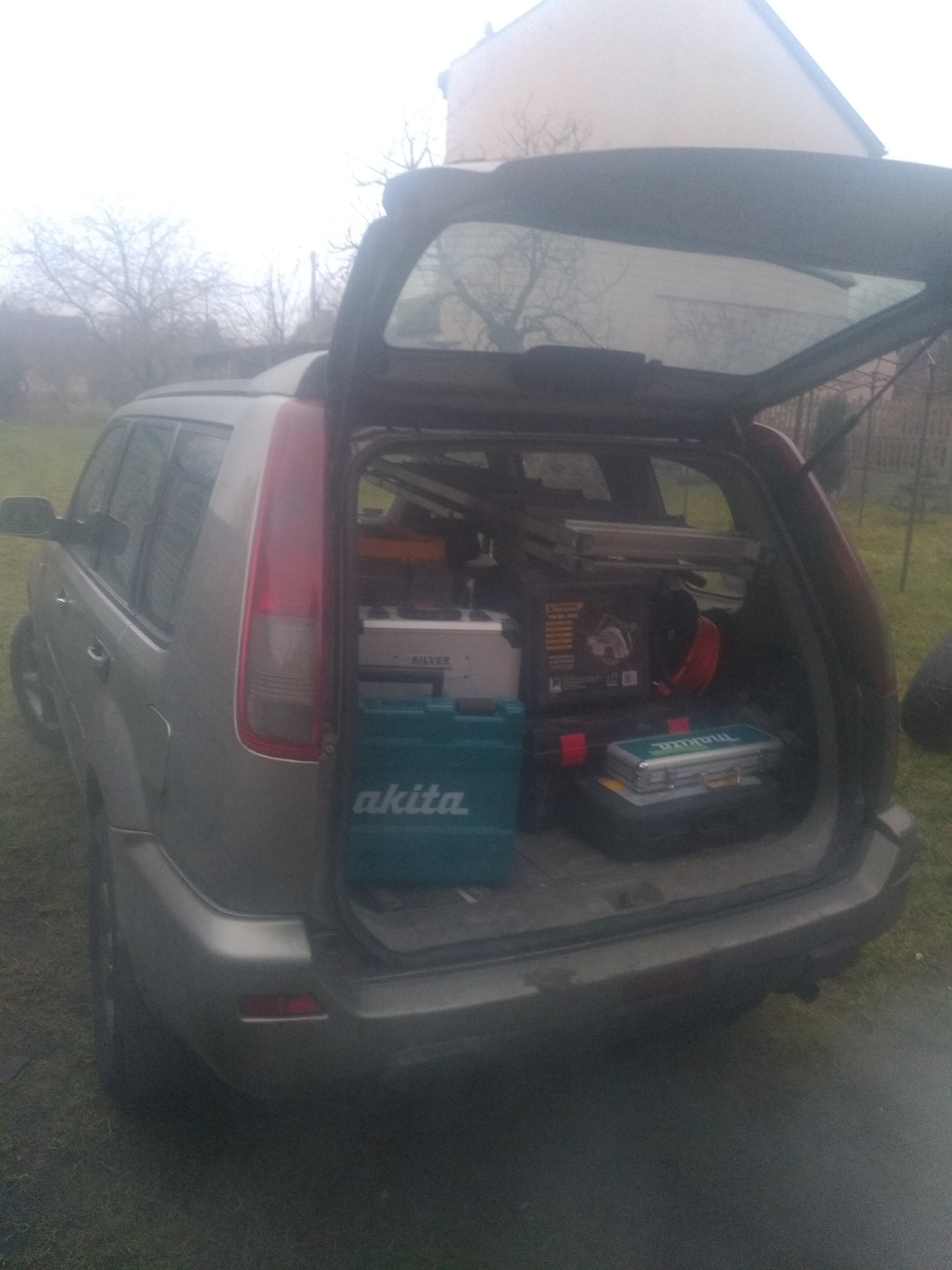Bagażnik samochodu typu SUV załadowany skrzynkami narzędziowymi marek Akita i Makita oraz innymi narzędziami i materiałami, prawdopodobnie przygotowanie do pracy.