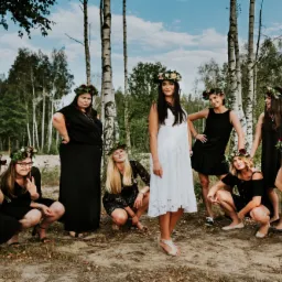 Grupa kobiet w sukienkach i wiankach na głowach, pozujących w lesie brzozowym, z dekoracją balonową w tle.