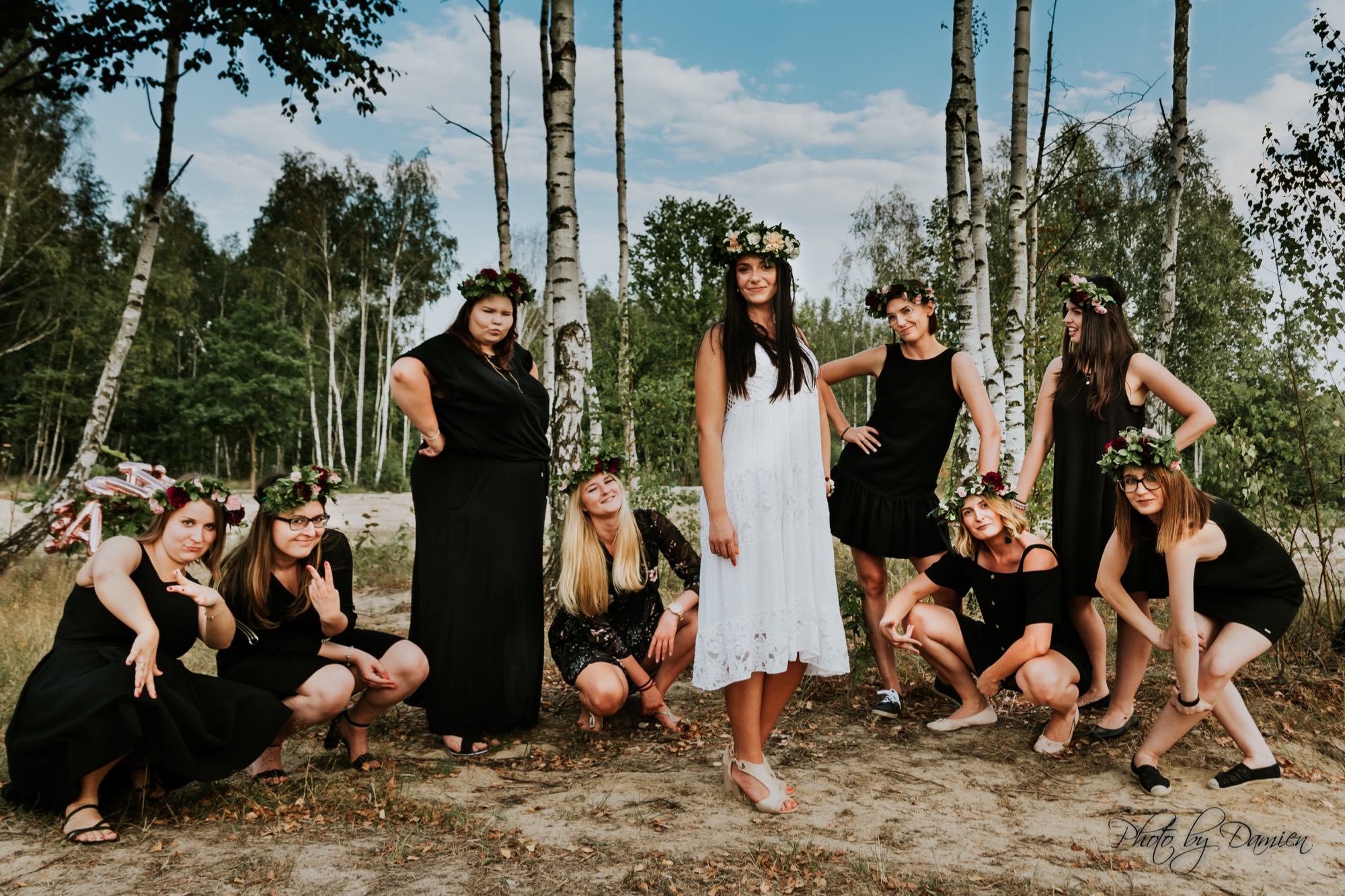 Grupa kobiet w sukienkach i wiankach na głowach, pozujących w lesie brzozowym, z dekoracją balonową w tle.