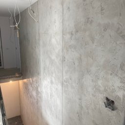 PRO Realizacja - Ściana z efektem dekoracyjnym w odcieniach szarości, widoczne kable zwisające z sufitu i przygotowane gniazdko elektryczne, fragment schodów w tle
