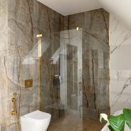 PRO Realizacja - Nowoczesna łazienka w odcieniach beżu i bieli z marmurowymi płytkami, złotymi akcentami armatury i kabiną prysznicową typu walk-in, wisząca toaleta z bidetką i subtelny akcent roślinny.