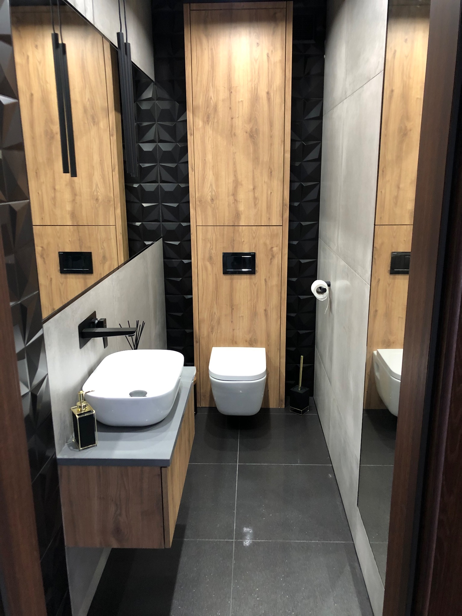 Nowoczesna łazienka w Bielawie z drewnopodobnymi panelami, czarnymi trójwymiarowymi płytkami, wiszącą toaletą i umywalką nablatową, oświetlona wiszącymi lampami.