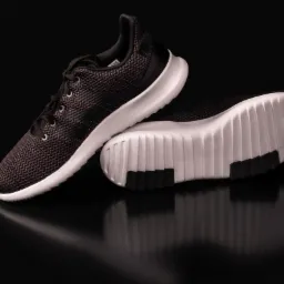 Para czarno-białych butów sportowych z trzema paskami na czarnym, błyszczącym tle, widoczne odbicie.