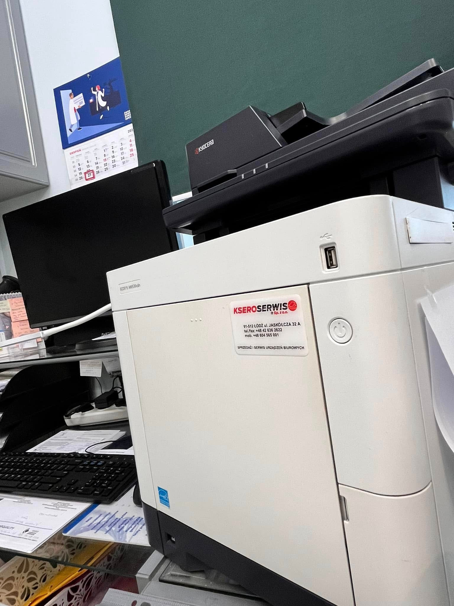 Kserokopiarka Kyocera ECOSYS M6530cdn na biurku w Łodzi, z widoczną naklejką firmy KSEROSERWIS i kalendarzem na ścianie.
