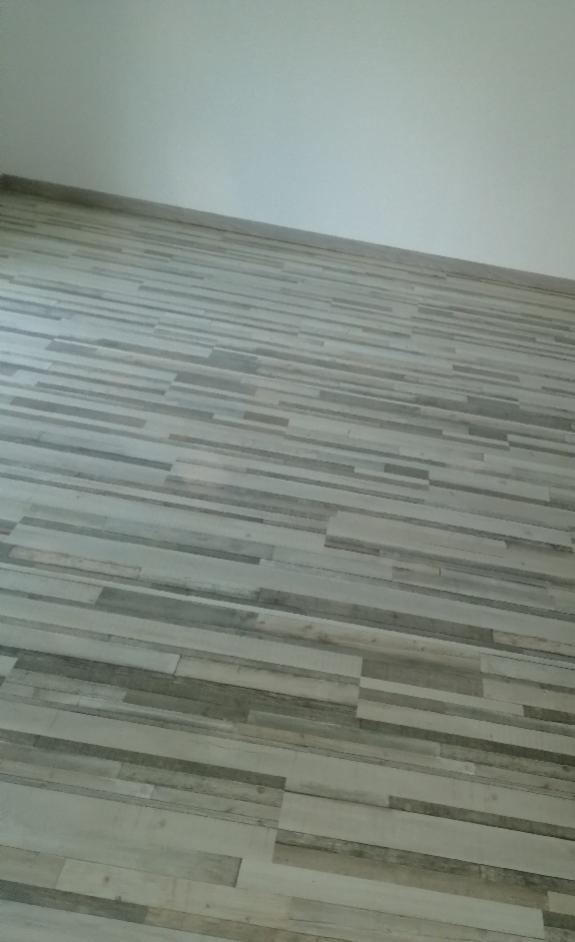 Ułożona podłoga z paneli imitujących drewno w odcieniach szarości i beżu, widok z góry pod kątem.