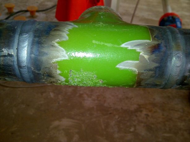Spoina na rurze w kształcie litery T, z zieloną farbą i śladami szlifowania, ukazująca proces obróbki metalu.