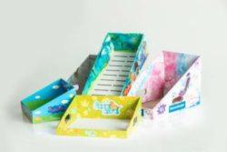 Ręcznie robione, kolorowe, tekturowe pudełka i tace z dziecięcymi motywami, ustawione na białym tle, prezentujące różnorodne wzory i kształty.