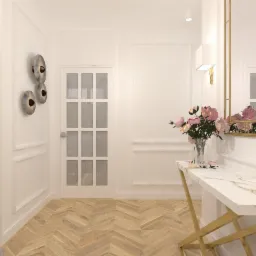 Elegancki przedpokój w jasnych barwach z parkietem w jodełkę, konsolą z marmurowym blatem i złotymi nogami, lustrem w złotej ramie oraz dekoracyjnymi lampami ściennymi.