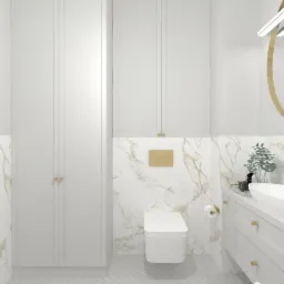 Elegancka, minimalistyczna łazienka z białymi szafkami, umywalką nablatową, złotymi akcentami i marmurowymi płytkami na ścianach; widoczna toaleta i lustro z oświetleniem LED.