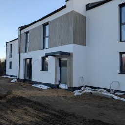 Nowoczesny dom z białą elewacją i drewnianymi panelami, widok z zewnątrz, teren wokół domu w trakcie prac wykończeniowych.