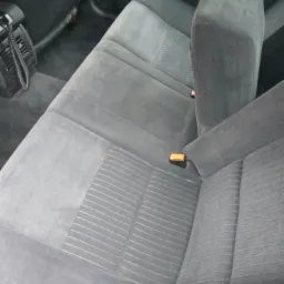 Szare, materiałowe siedzenia samochodowe z widocznymi pasami bezpieczeństwa, po czyszczeniu, widoczne delikatne wzory na tapicerce.