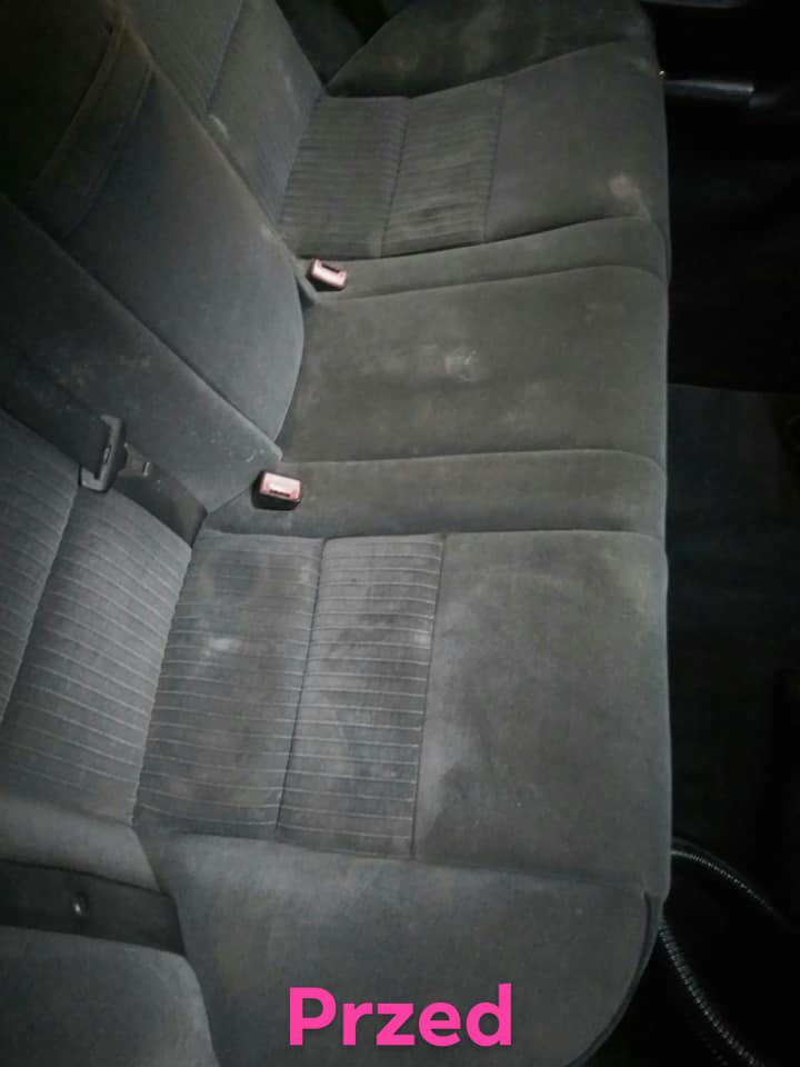 Szare, materiałowe siedzenie samochodowe z widocznymi plamami i zabrudzeniami, z napisem 'Przed' w dolnej części kadru.