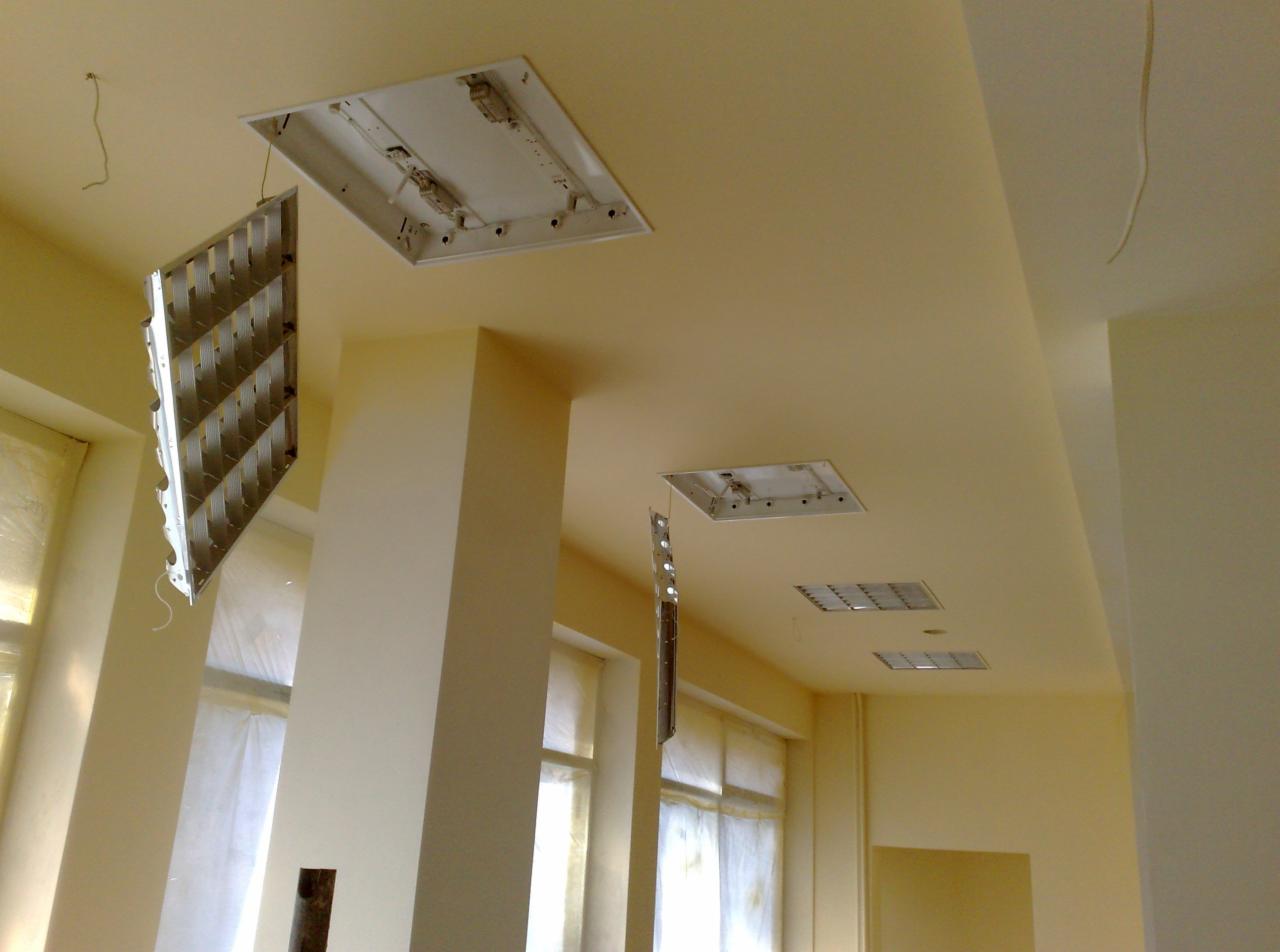 Remont wnętrza: odsłonięte oprawy oświetleniowe w suficie, widoczne okna z zasłonami, świeżo pomalowane ściany w odcieniach beżu i kremu.