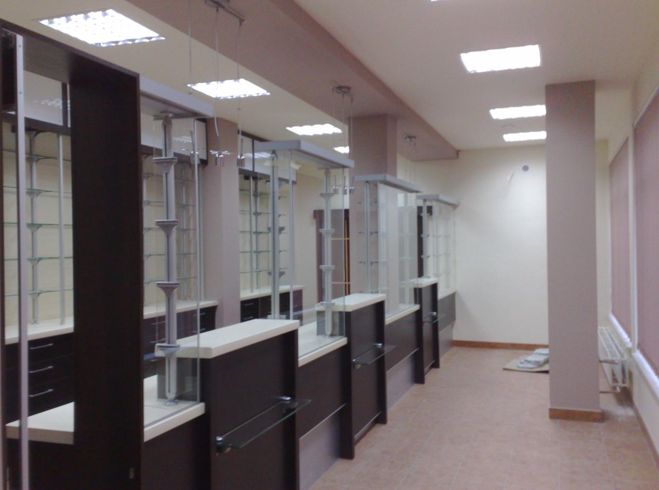 Nowoczesne, brązowo-białe witryny sklepowe z szklanymi półkami i elementami dekoracyjnymi, ustawione w rzędzie w jasnym pomieszczeniu z brązowymi akcentami.