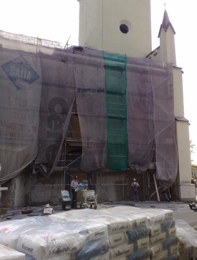 Renowacja elewacji kościoła w Myszkowie: rusztowania, siatki ochronne, worki z zaprawą, tynkarze przy pracy, mieszarka. Detal: charakterystyczna wieża kościelna.