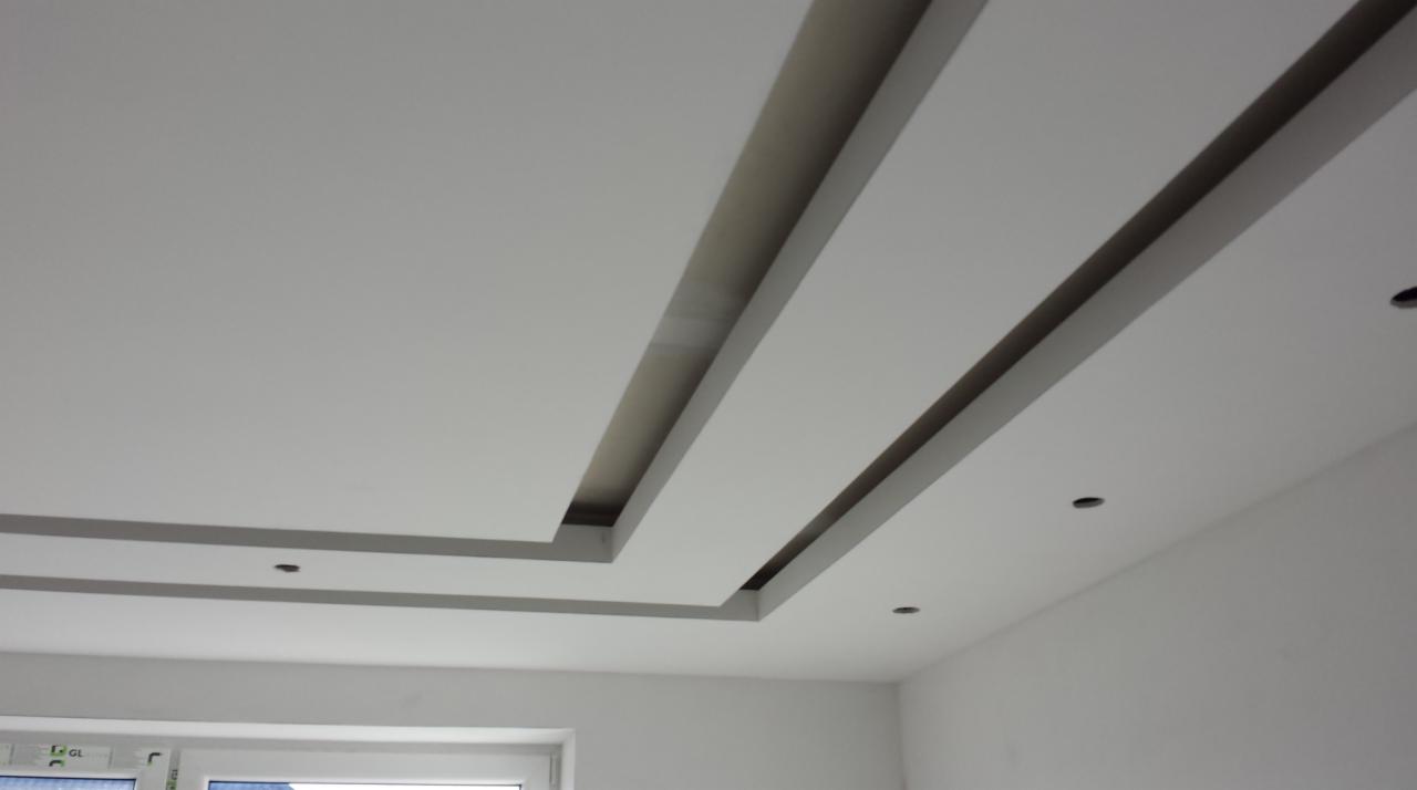 Gładki, biały sufit z dekoracyjnymi, podłużnymi wnękami oświetleniowymi i punktowymi lampami, widok z dołu, nowoczesne wykończenie.