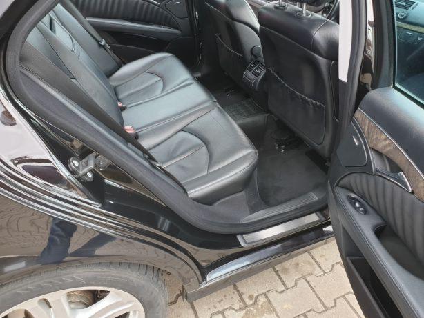 Wnętrze czarnego samochodu z otwartymi tylnymi drzwiami ukazujące skórzane siedzenia i dywaniki.