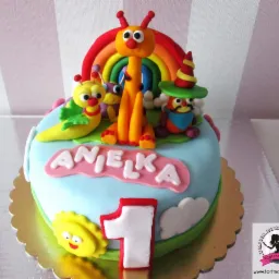 Tort urodzinowy dla dziecka z imieniem Anielka, zdobiony figurkami postaci z bajki i tęczą z lukru, na złotym podkładzie.