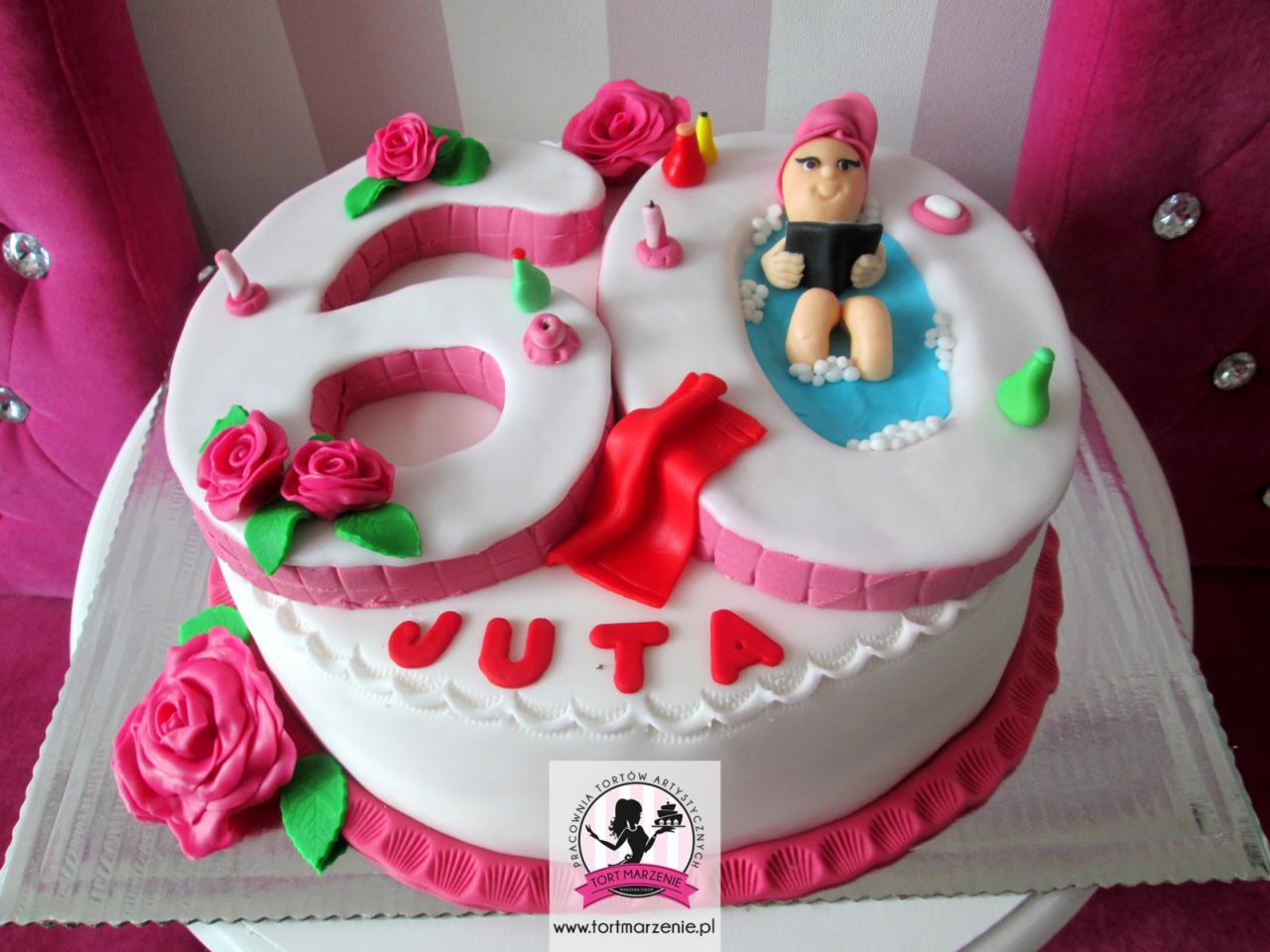 Ozdobny tort urodzinowy w kształcie liczby 60, dekorowany różami z lukru i figurką kobiety w wannie z książką, całość na srebrnej tacy.