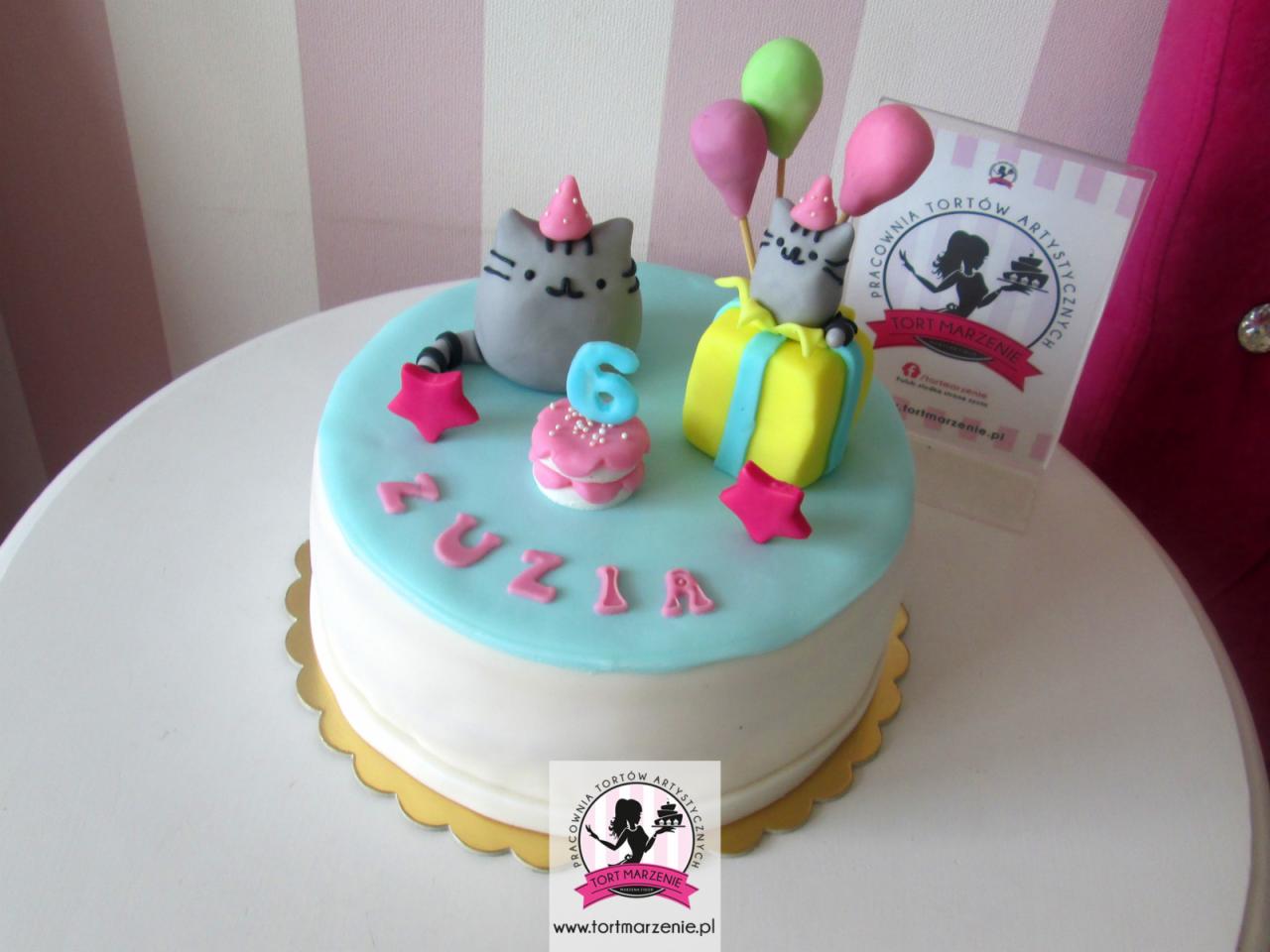 Tort urodzinowy dla dziecka z motywem kotów Pusheen, imieniem Zuzia i cyfrą 6, ozdobiony lukrem, gwiazdkami i balonami, na białym stole.