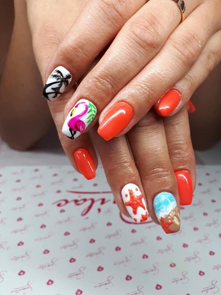 Dłonie z pomarańczowymi paznokciami i letnimi zdobieniami: palma, flaming, rozgwiazda i plaża na białym tle, na tle podkładki z logo salonu.