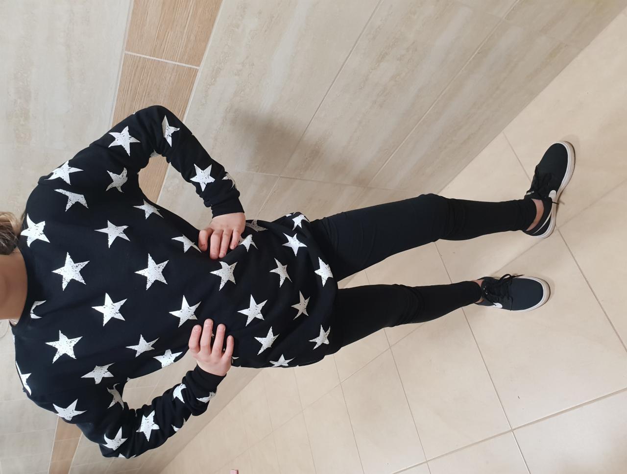 Dziewczynka w czarnej bluzie w białe gwiazdy i czarnych legginsach, pozująca na kafelkach.