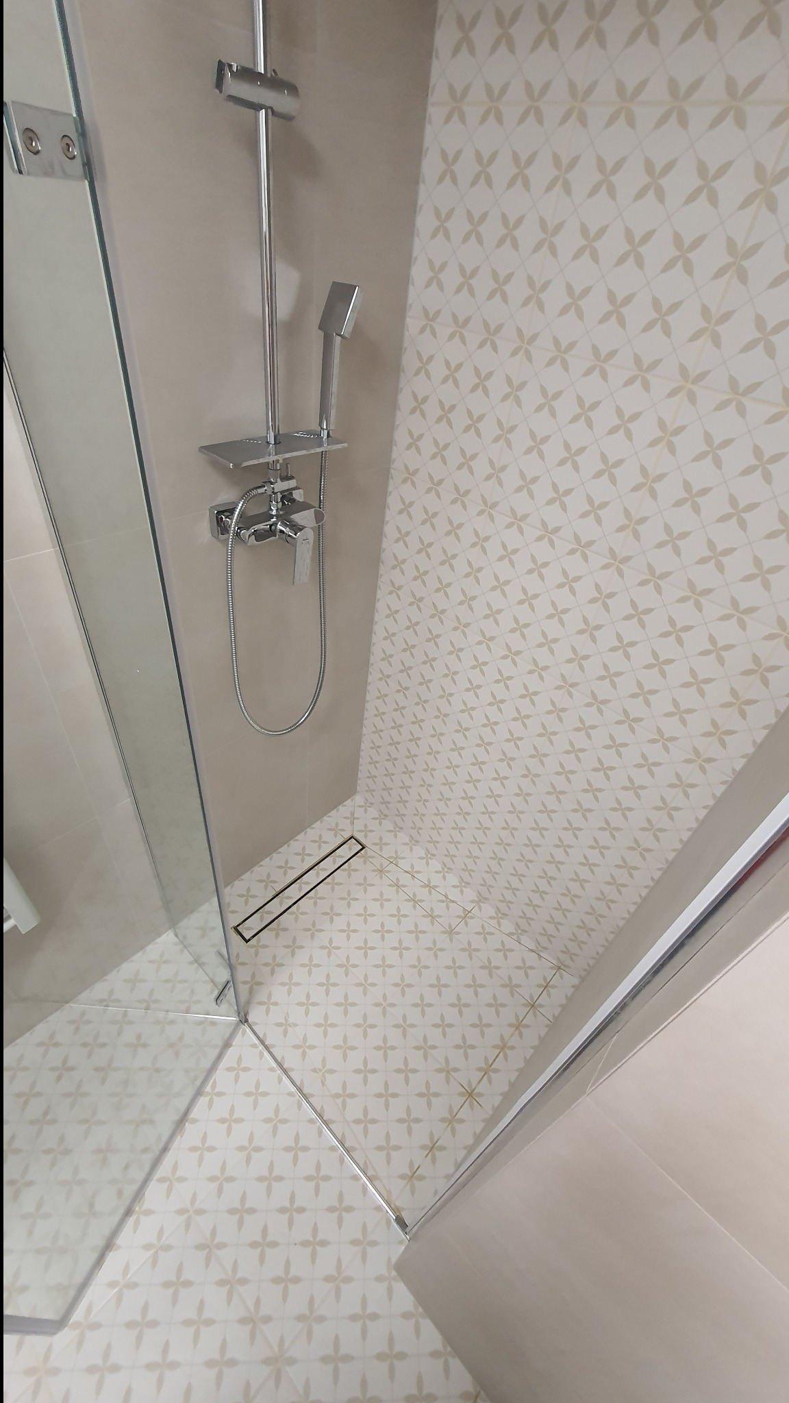 Nowoczesna kabina prysznicowa z odpływem liniowym i armaturą w chromie, wykończona płytkami w delikatny wzór. Widok z góry podkreśla estetykę i funkcjonalność.