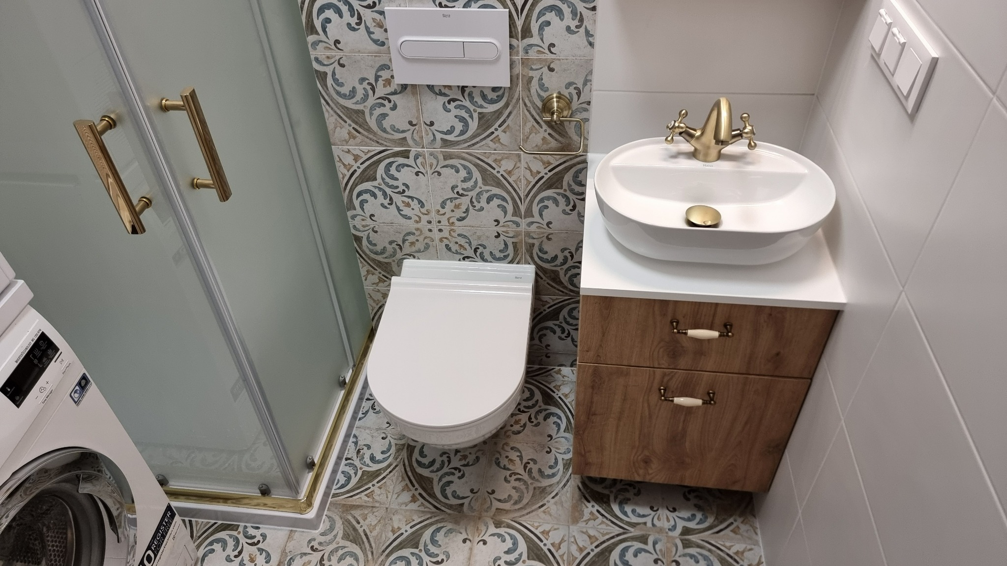 Nowoczesna łazienka po remoncie: kabina prysznicowa ze złotymi uchwytami, umywalka z szafką w stylu rustykalnym i toaleta. Płytki podłogowe i ścienne w stylu vintage.