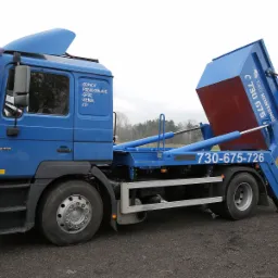 Niebieska ciężarówka z kontenerem na gruz w Ruminie, gotowa do załadunku, z widocznym numerem telefonu firmy.