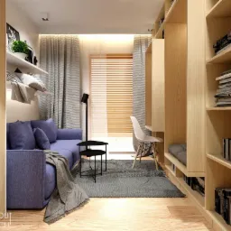 Kompaktowy pokój w Krakowie z niebieską sofą, stolikiem pomocniczym, drewnianymi regałami z wbudowanym biurkiem i białym krzesłem, oświetlony naturalnym światłem przez żaluzje.