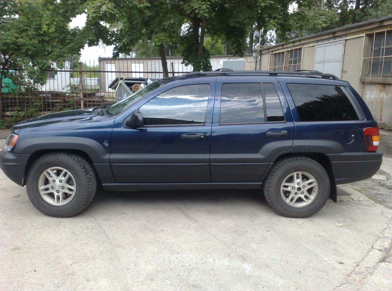 Niebieski samochód terenowy zaparkowany na betonowym podłożu, z widocznymi drzewami i budynkami w tle.