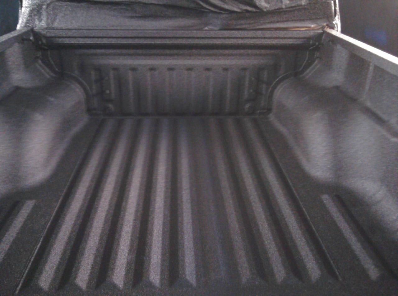 Wnętrze paki samochodu typu pickup pokryte szarą, chropowatą powłoką ochronną, widoczne rowki i detale wykończenia.