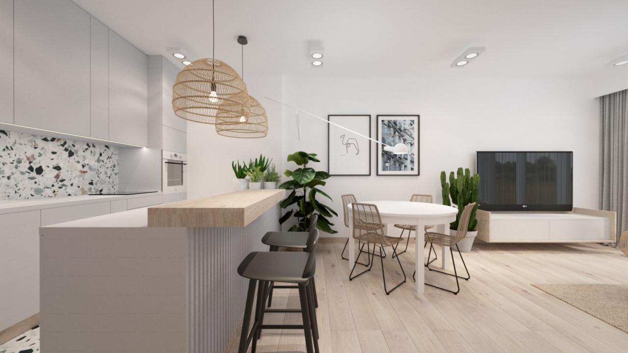 Wnętrze mieszkania z otwartą kuchnią, wyspą z hokerami, okrągłym stołem i telewizorem, oświetlone wiszącymi lampami z abażurami z naturalnego materiału.