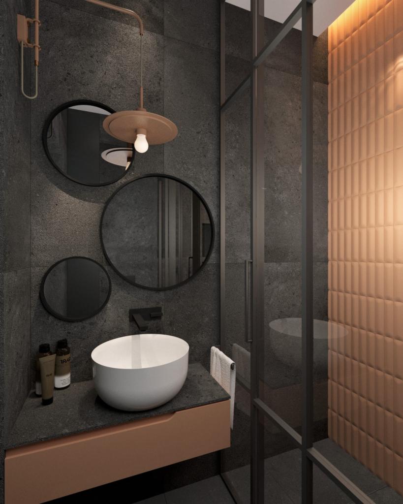 Nowoczesna łazienka z umywalką nablatową, trzema okrągłymi lustrami, miedzianą lampą i kabiną prysznicową z czarnymi profilami na tle ciemnoszarych płytek.