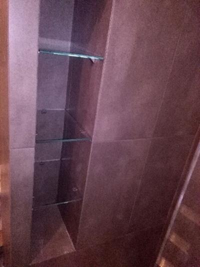 Wbudowana szafka z brązowymi płytkami i szklanymi półkami, widok z dołu.