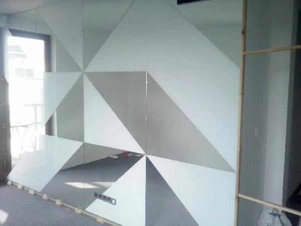 Montaż dekoracyjnej ściany lustrzanej z geometrycznym wzorem trójkątów, widoczne elementy mocujące i odbicie pomieszczenia.