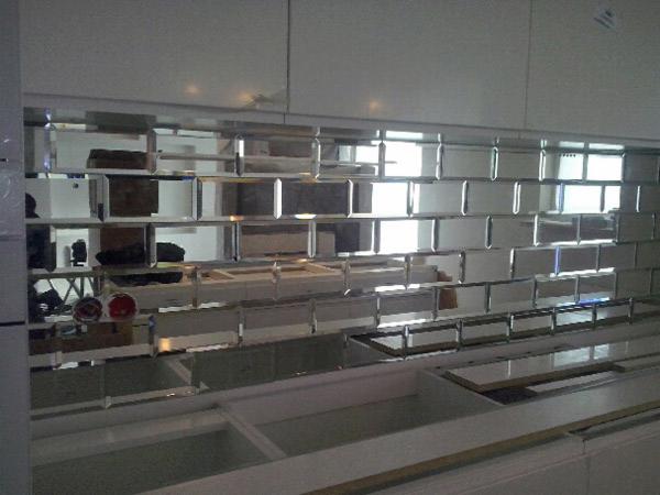 Ściana w kuchni wyłożona lustrzanymi płytkami w kształcie cegiełek, odbijającymi światło, z widocznymi elementami zabudowy kuchennej w dolnej części kadru.