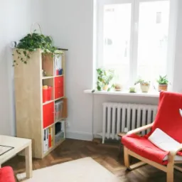 Jasne wnętrze gabinetu z czerwonym fotelem, regałem wypełnionym książkami i roślinami doniczkowymi na parapecie okna.