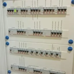 Rozdzielnica elektryczna z bezpiecznikami, widoczne opisy obwodów i jeden włączony bezpiecznik z zieloną diodą.