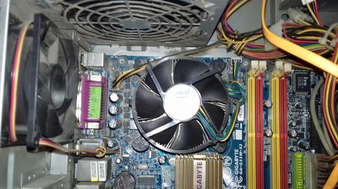 Wnętrze brudnej obudowy komputera stacjonarnego z widoczną płytą główną Gigabyte GA-G33M-S2, chłodzeniem procesora Intel, pamięcią RAM DDR2 (czerwone i żółte sloty) oraz licznymi kablami.