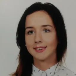 Portret młodej kobiety z ciemnymi włosami i delikatnym uśmiechem, ubrana w białą koszulę z drobnym wzorem na jasnym tle.