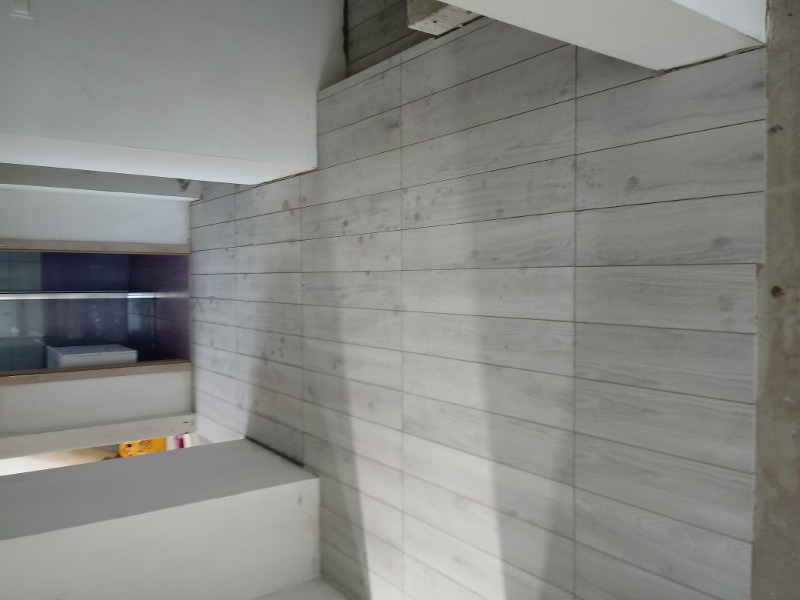 Ściana wyłożona jasnymi, podłużnymi płytkami imitującymi drewno, widoczne półki z wyposażeniem w tle.